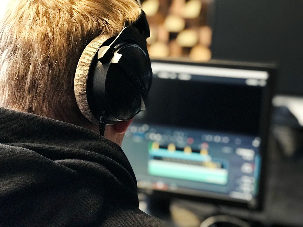 Ein Komponist mit Studiokopfhörern bearbeitet einen Track in einer digitalen Audio-Workstation.
