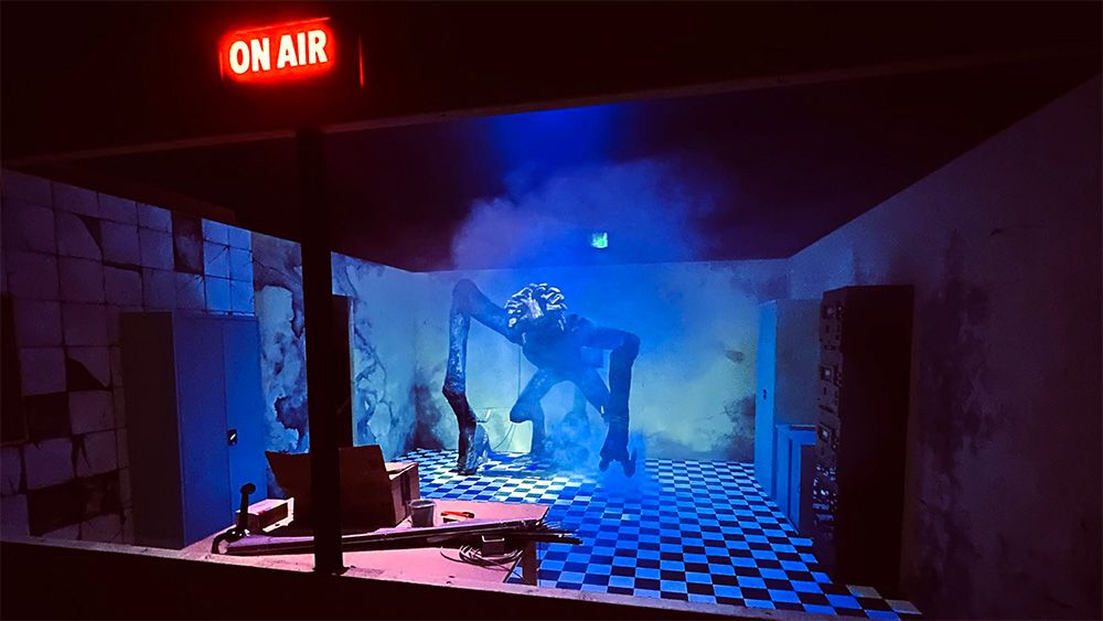 Eine monströse Animatronic-Kreatur ragt in einem nebligen Kulissen-Set mit Schachbrettboden und leuchtendem „ON AIR“-Schild auf.